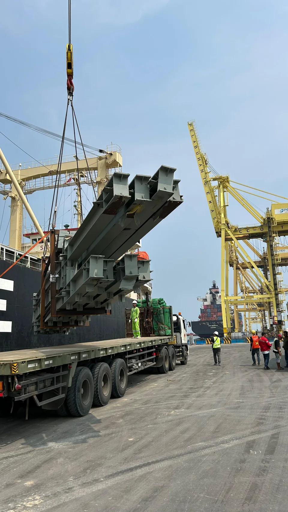 Aktivitas pengangkatan kargo struktur baja di area dermaga.