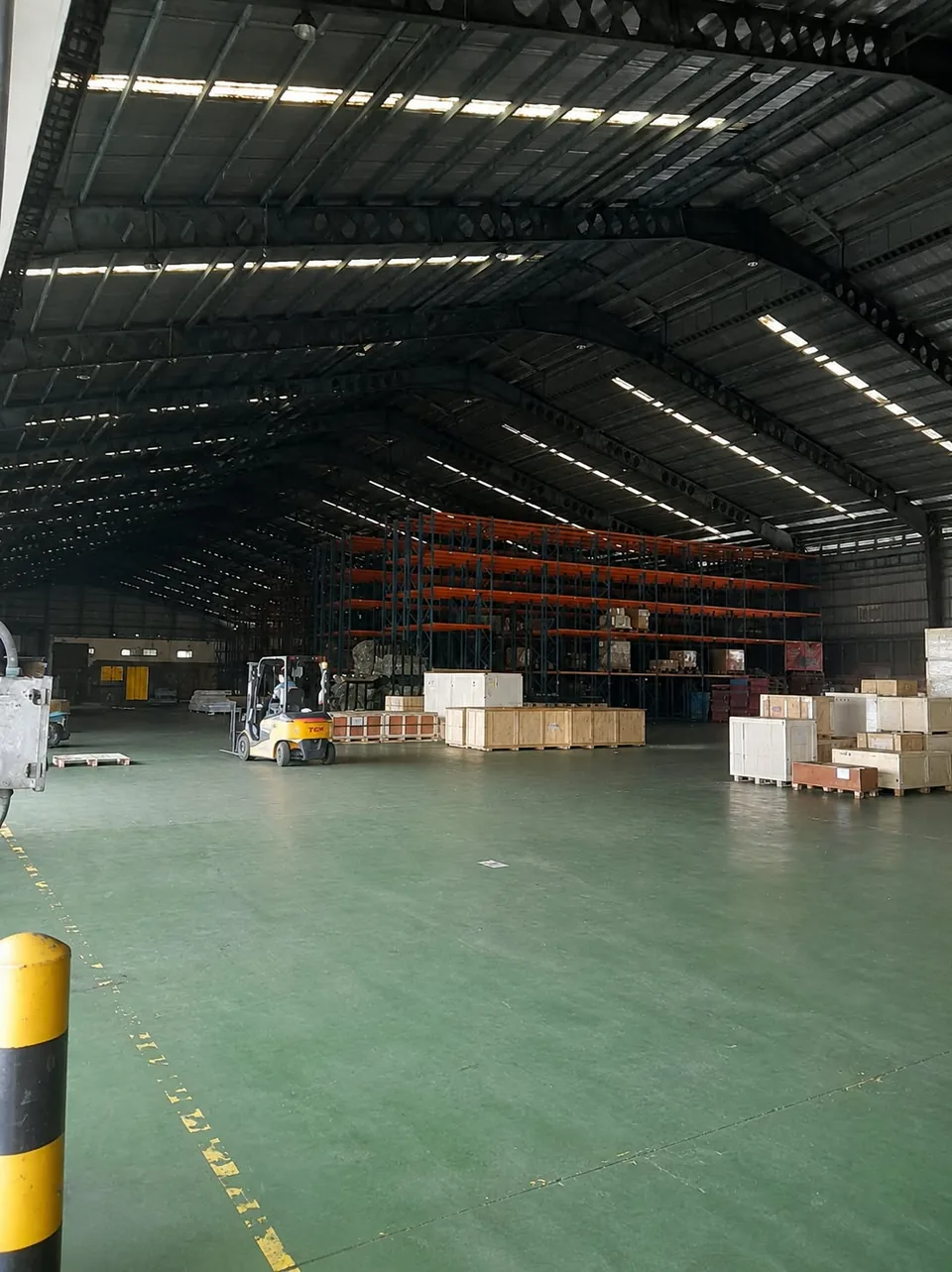 Area gudang dengan rak, barang tersusun, dan forklif.